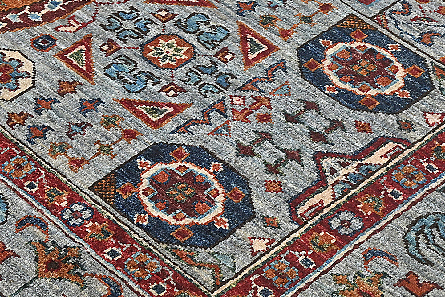 Close-up of a patterned rug with geometric designs in red, blue, and brown on a gray background.