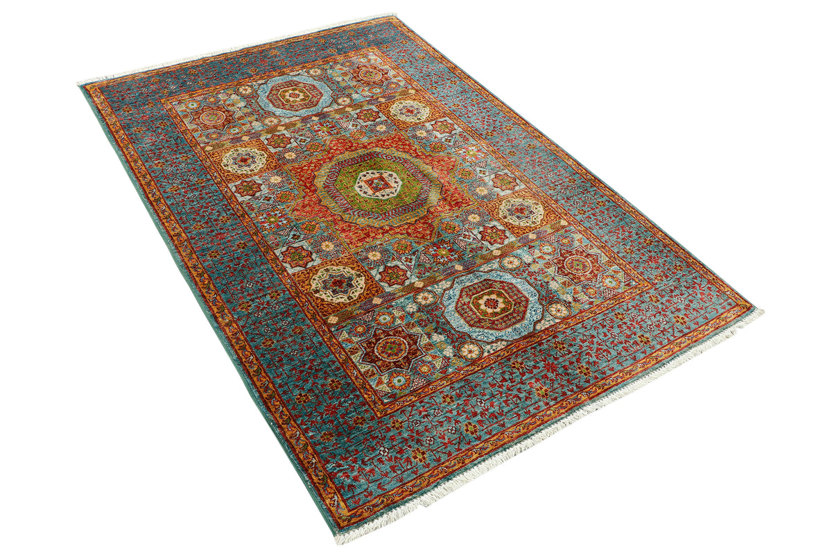 A rectangular traditional area rug with an intricate floral and geometric pattern, featuring a dominant blue-gray field, a rust-red central medallion, and white fringe on the ends, shown from an elevated angle on a white background.