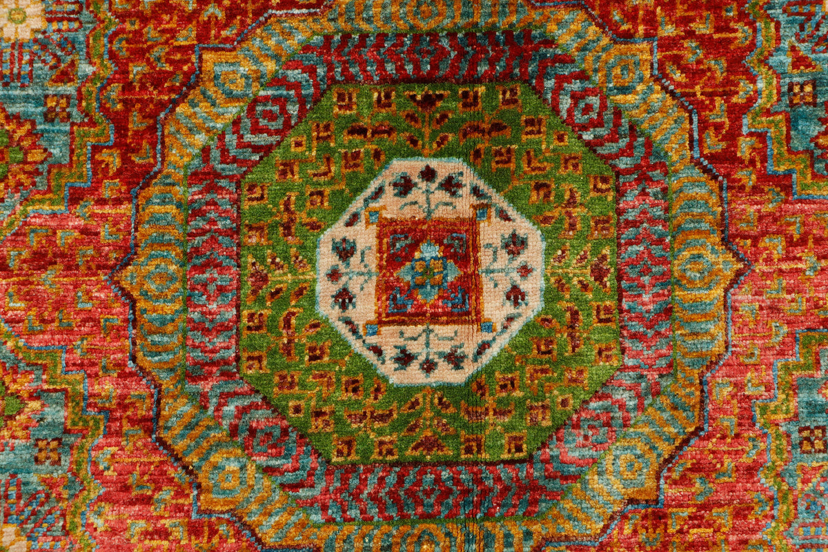 A close-up of a traditional patterned rug with a central octagonal medallion and concentric bands of red, green, blue, and cream motifs.