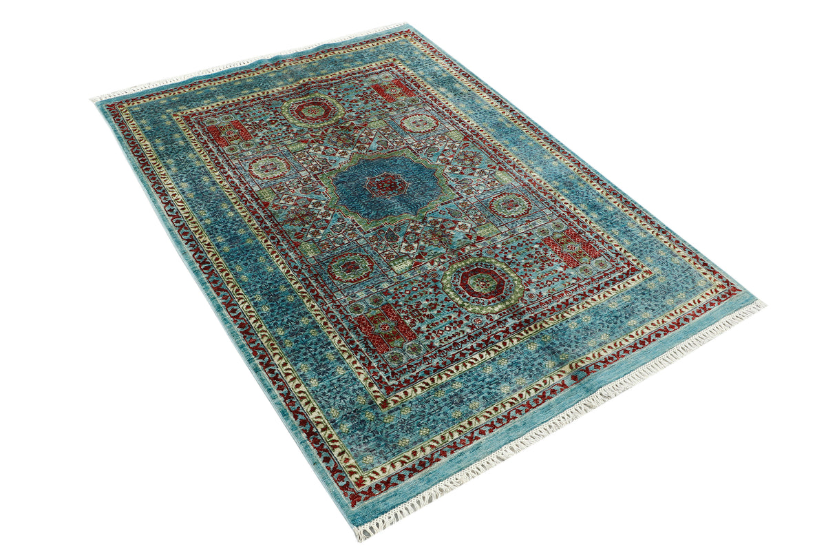 A rectangular traditional area rug with a complex geometric and floral pattern, featuring a dominant turquoise blue field, red and gold central medallions, and cream fringe on the ends, shown from an elevated perspective against a white background.