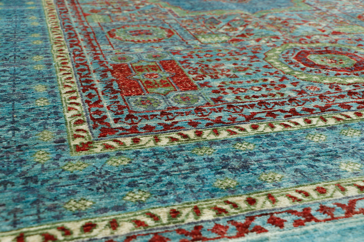 A close-up view of an ornate area rug with a distressed blue field, featuring red, beige, and green geometric and floral motifs.