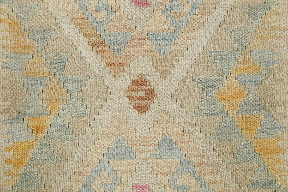 Close-up of a woven textile pattern with geometric diamond and chevron motifs in beige, pale blue, mustard yellow, and soft pink.