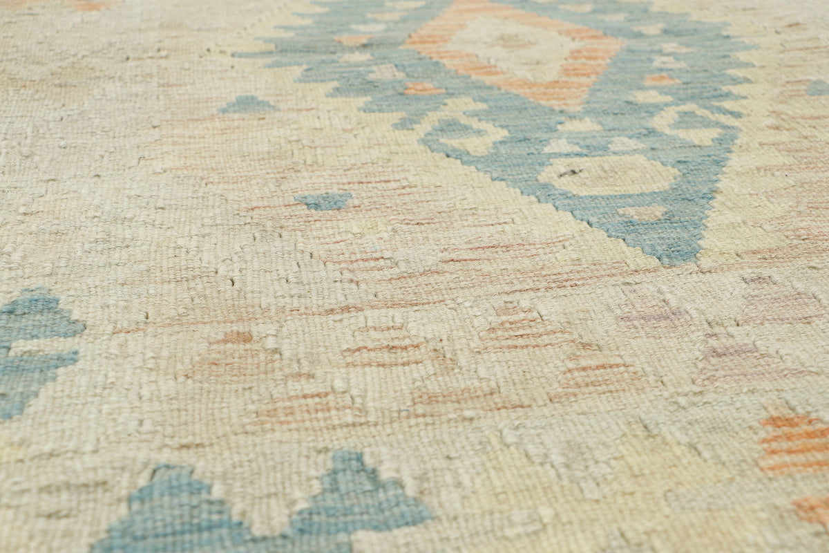 Close-up of a woven rug with a cream base and geometric patterns in muted blue, peach, and beige.
