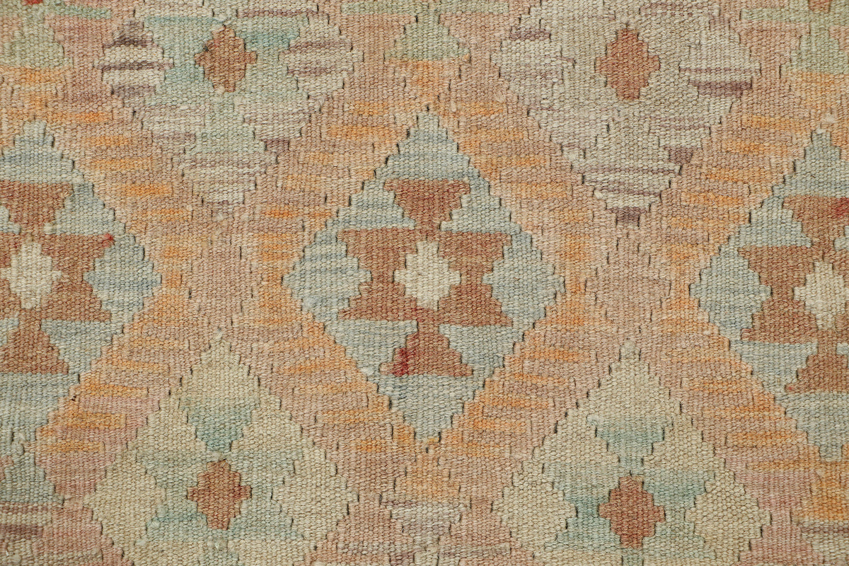 A close-up of a woven textile with a geometric diamond pattern in muted peach, beige, pale blue, and brown tones.