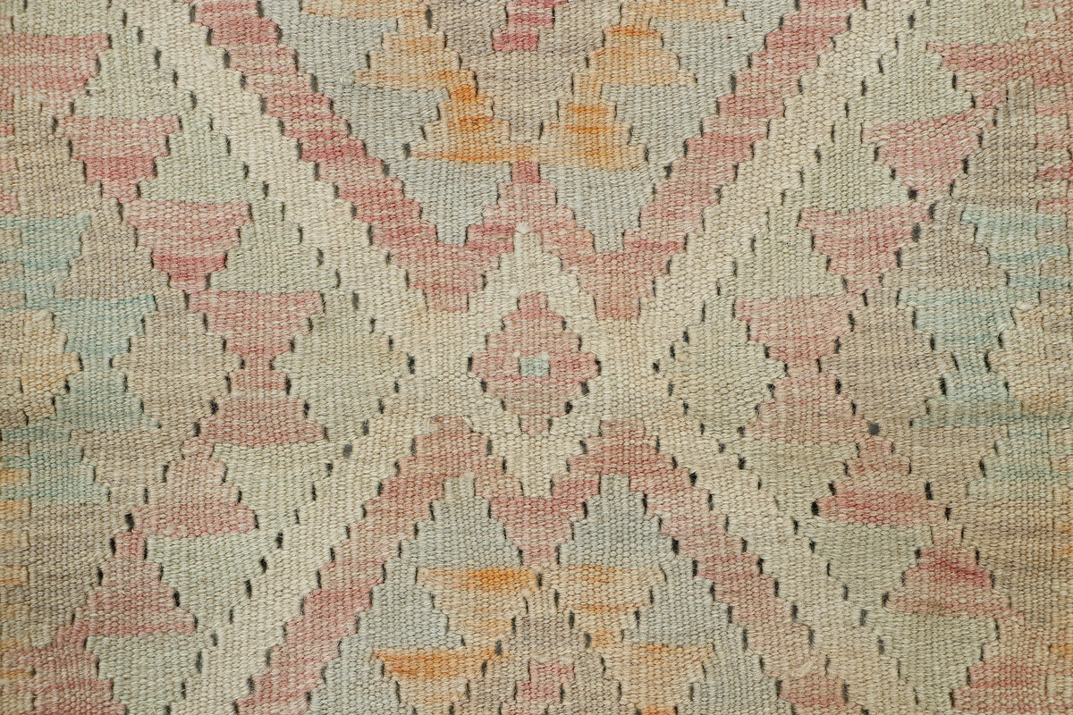 A close-up of a woven textile with a geometric diamond pattern in muted pink, peach, orange, pale blue, and beige tones.