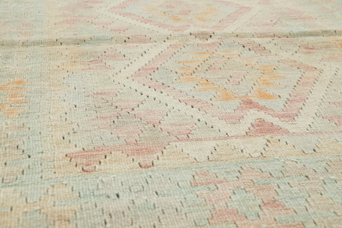 Close-up of a woven rug with a geometric diamond pattern in soft pastel tones of pink, beige, light blue, and muted orange.