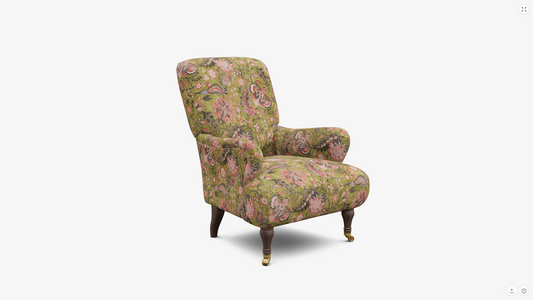 An upholstered armchair with a dense floral pattern in muted green, pink, and beige tones, featuring dark wooden legs with gold-toned casters, shown against a plain white background.