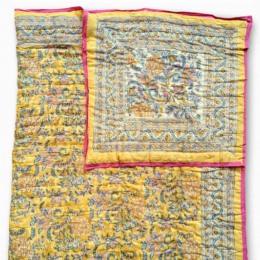 Yellow floral patterned quilt with pink border on a white background