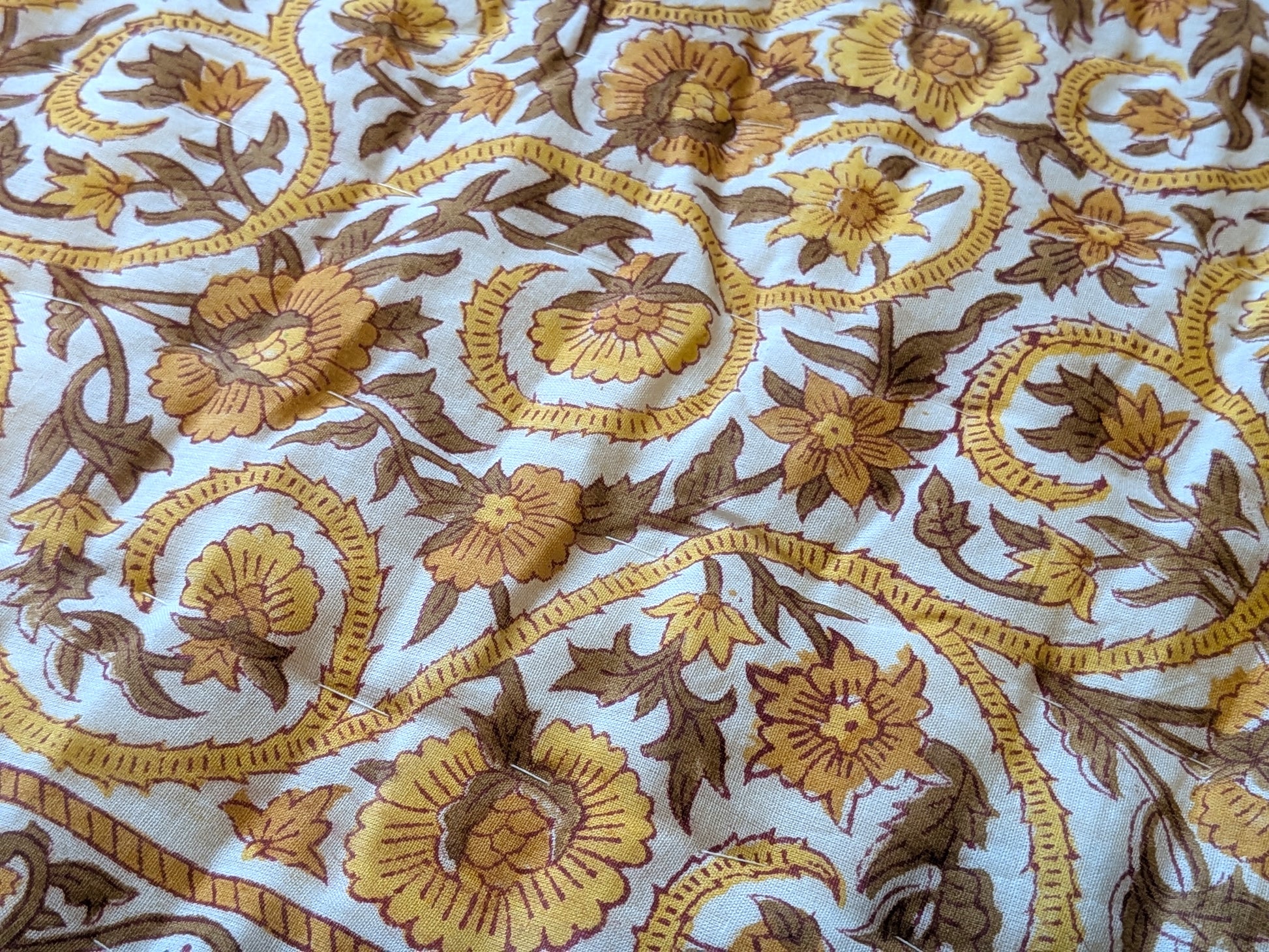 Close-up of embroidered fabric with floral patterns in brown and yellow on a white background