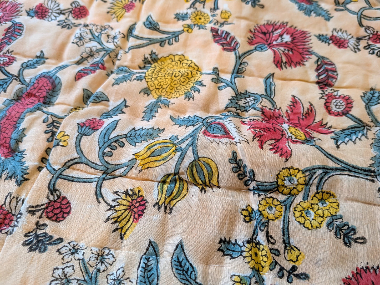 Close-up of floral patterned fabric with red, yellow, and blue colors on a beige background.