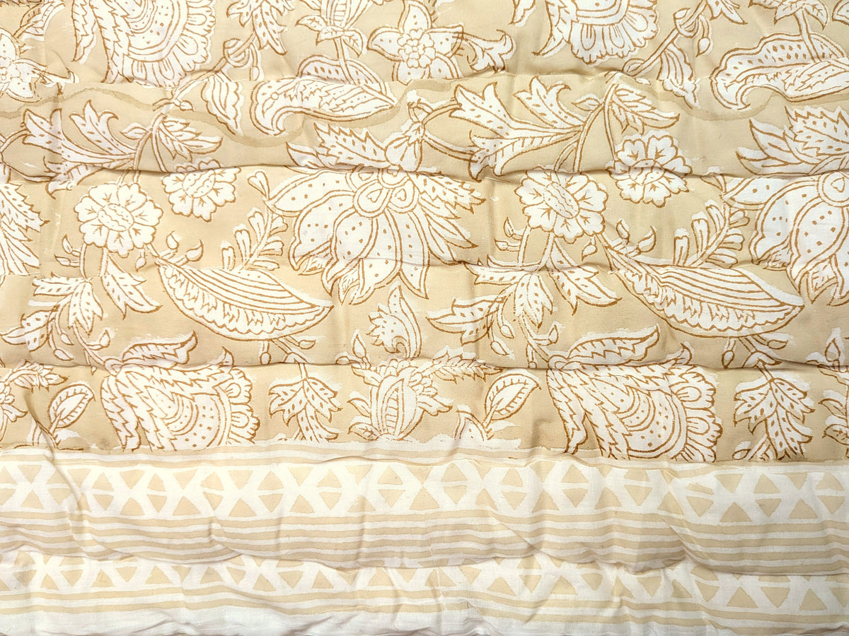 A close-up of a quilted fabric with a beige and cream floral paisley pattern and a decorative geometric border at the bottom.