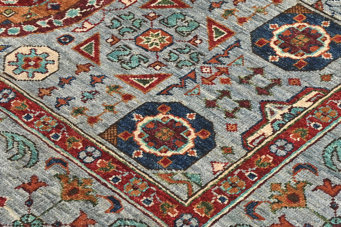 Close-up of a patterned rug with geometric designs in red, blue, and beige on a gray background.