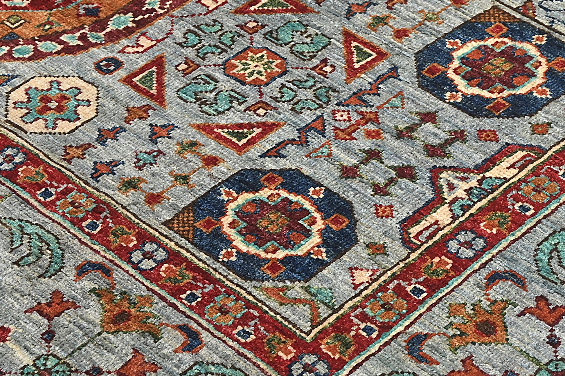 Close-up of a patterned rug with geometric designs in red, blue, and beige on a gray background.