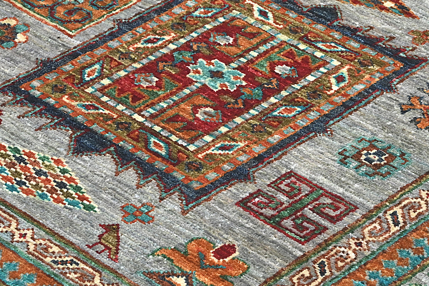 Close-up of a patterned rug with geometric designs in red, orange, and blue on a gray background.